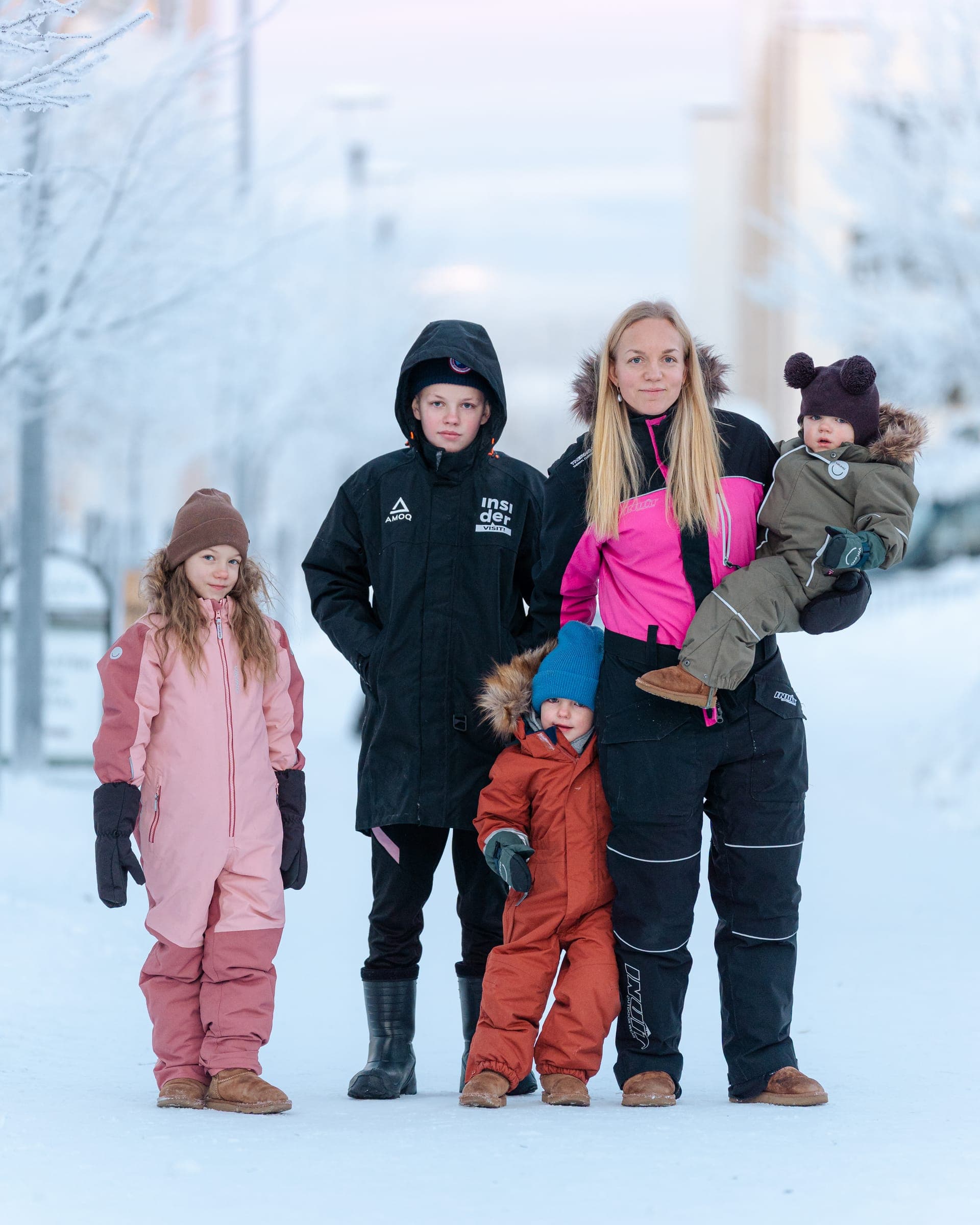 A family of five dressed in winter overalls and jackets on a snowy street